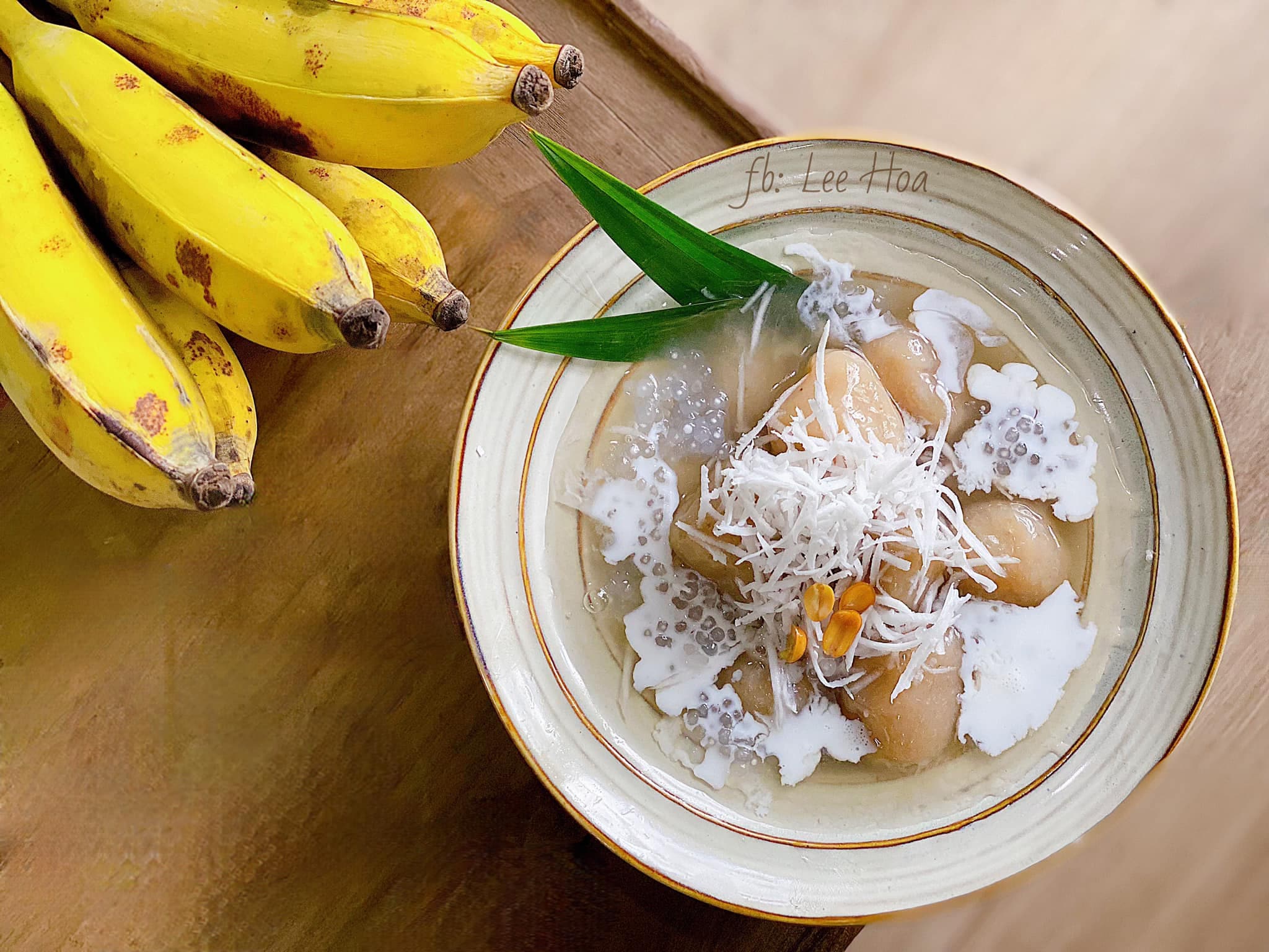 A bowl of golden che chuoi topped with roasted peanuts and coconut flakes, steam rising from the warm coconut milk base